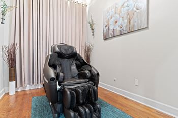 A massage chair sits in the corner of a room with a painting on the wall